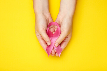 Breast cancer concept. Female hands with pink ribbon on yellow background