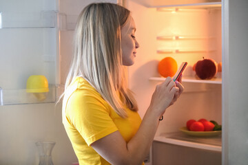 Young woman opened the refrigerator and makes an application for the purchase and delivery of...