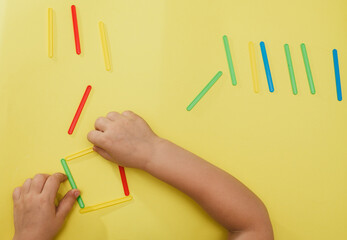 A small child collects a geometric figure from counting sticks. Children's hands with counting sticks isolated on a yellow background.