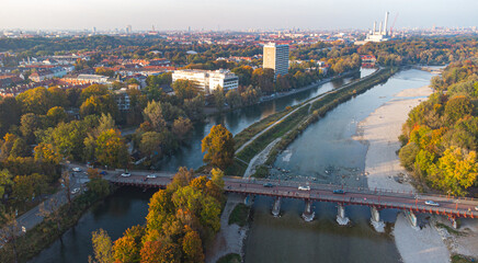 Fototapeta premium Aerial view of Isar river flowing into Munich and Thalkirchen bridge with cars in a beautiful autumn landscape