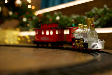 Vintage train is on the floor under a decorated Christmas tree on the background of a garland of bokeh lights. The concept of celebrating Christmas and New Year.