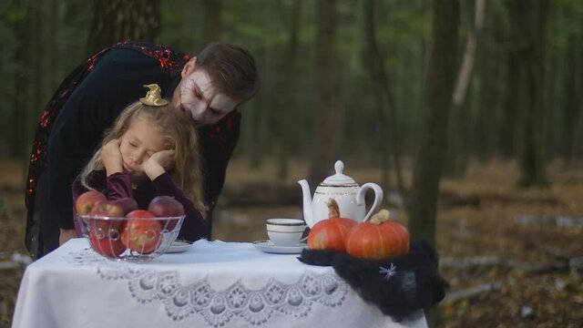 Young man with face paint in vampire costume trying scare little bored girl sitting in forest on Halloween. Caucasian brother having fun with sister outdoors in woods. Traditional holiday celebration