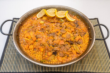 Great Spanish vegetable paella presented in its paella pan with lemon to garnish and with its socarrat