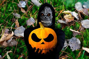 Close-up portrait of grim reaper. Man in death mask with fire flame in eyes on on nature green moss...