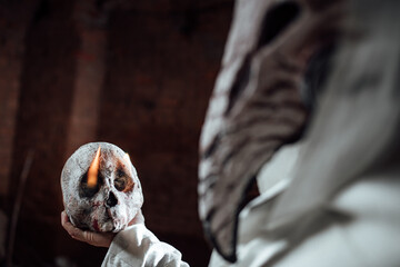 a man dressed as a plague doctor holds a human skull in his hand. costume party for Halloween....
