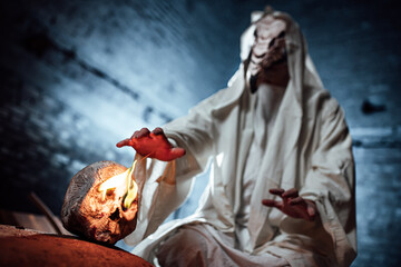 the plague doctor. cosplay of a gloomy image for Halloween. a mask with a bird's beak and a white hoodie. a masked man stretches his hands towards a human skull with burning eyes