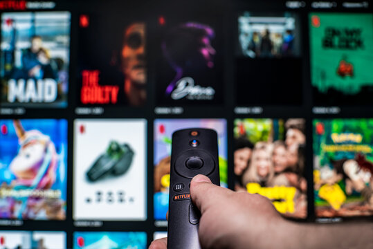 Uzhgorod, Ukraine. October 19, 2021 Man watches movies on Netflix. Internet television. The human hand, includes the remote control of the film screen in the blurr.  TV.