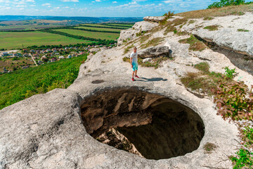 A young man on the edge of a precipice in the form of a huge hole in the ground among green fields...