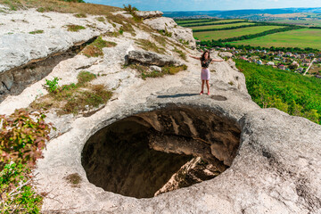 A young woman on the edge of a precipice in the form of a huge hole in the ground among green...