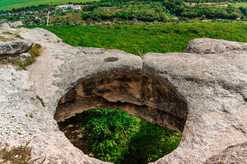 Panoramic view of huge hole in ground among green field and mountain on sunny summer day in Crimea. Abnormal cave, failure in ground. Anomaly grotto.
