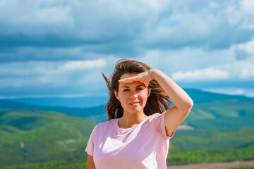 A young woman on the top of a mountain on a sunny summer day and admiring the mountain landscape....