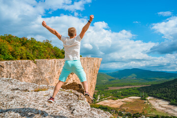 A happy young man on top of a mountain jumps with his hands open. The concept of achieving goals and success