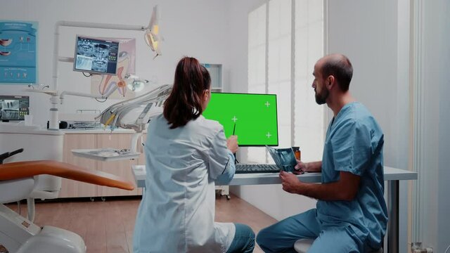 Dentistry team analyzing teeth x ray and green screen on monitor at dentist office. Specialist and man nurse working with isolated mockup template and radiography for teethcare.
