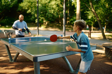 Father and son play table tennis outdoors - obrazy, fototapety, plakaty
