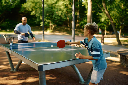 Father and son play table tennis outdoors