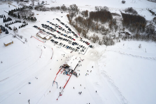 Aerial View Of The Ski Lift At The Foot Of The Ski Slope With A Crowd Of Skiers And Snowboarders. There Is A Parking Lot Next To The Lift.