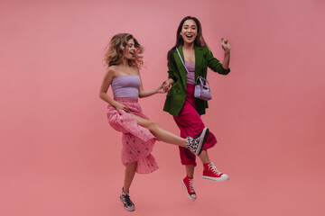 Attractive young women of asian and european appearance dancing and laughing in front of pink...
