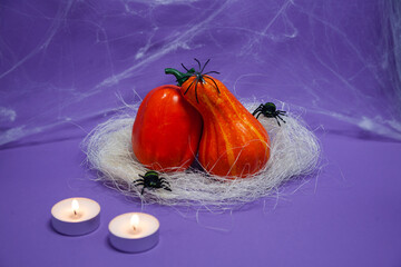 Halloween, decoration and holidays concept - Two small pumpkins of different kinds on straw bent over each other with crawling spiders, lit candles and cobwebs on a purple background with copy space
