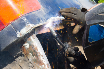 Worker in helmet repair detail in car service