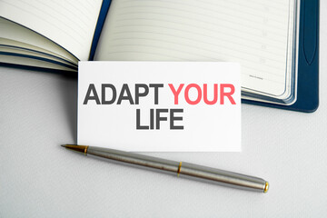 Business concept. Text adapt your life writing on paper card, notebook on wooden background.