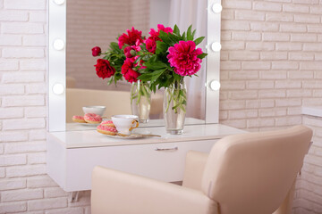 Client place in hairdressing beauty salon with cup of tea, donuts and peonies flowers