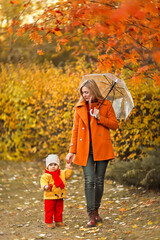 young girl with a child walks under an umbrella in an autumn park