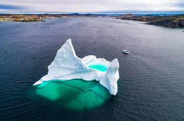 Giant iceberg near shore dwarfs a boat sailing past