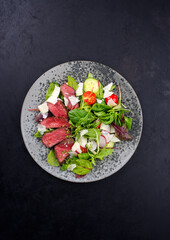 Modern style traditional fried dry aged bison beef rump steak slices with vegetable, lettuce and parmesan cheese served as top view on a design plate with copy space