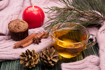 Cupcake on the background of a knitted winter sweater and a cup of tea. Christmas tree twig, cinnamon and cones