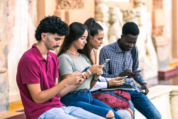 Group of multiracial people using the mobile sitting outdoors