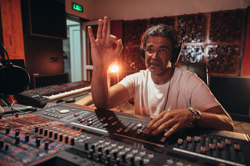 Senior hispanic music producer working on a mixing soundboard while in his studio