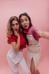 Surprised young racial teenagers girls shocked by what they saw on pink background. Studio shot models from europe and asia in colorful T-shirts posing together. Lifestyle leisure and beauty concept.