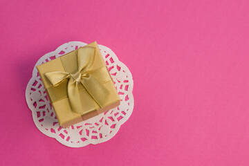 Closed golden gift box with silk gold ribbon bow on bright pink background