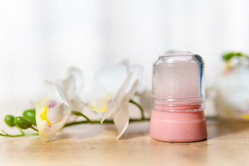 Obraz na płótnie Canvas Natural eco crystal alum deodorant and orchid branch with flowers on light wooden background