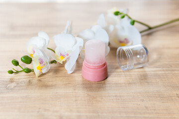Fototapeta na wymiar Natural eco crystal alum deodorant and orchid branch with flowers on light wooden background
