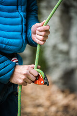 Hands of a climber holding a belay device and a rope while belaying a lead climber.