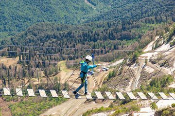 Young boy walks on a suspension bridge at Caucasian mountains. Rosa peak, spring. Sochi, Krasnaya polyana.