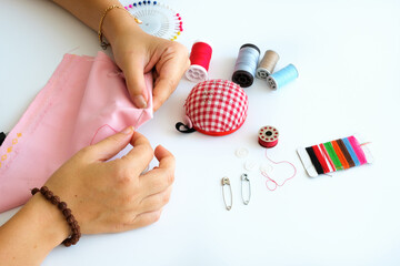 Tailor hands working with needle and thread, woman with sewing concept on white background. Beautiful top view of female tailor hands with equipment for sewing waiting on the table.