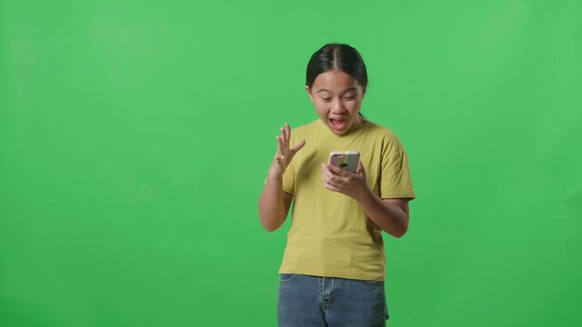 Young Asian Kid Girl Surprise And Say Wow During Use Mobile Phone While Standing On Green Screen In The Studio
