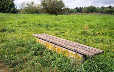 Simple bench in the grass diagonally across the image. The photo was taken in a Dutch nature reserve on a cloudy day at the end of the summer season.