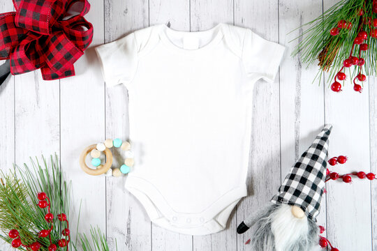 Baby romper jumpsuit onesie product mockup. Christmas farmhouse theme SVG craft product mockup styled with gift with buffalo plaid bow and farmhouse style gnomes against a white wood background.