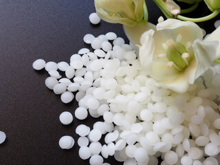 A pile of natural white beeswax pearls on a black background and white natural flower