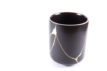 Isolated Japanese kintsugi cup restored with real gold , black pottery with gold cracks