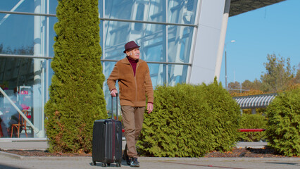 Elderly old retired grandpa tourist go to international airport terminal for boarding on plane for traveling. Stylish senior mature grandfather carrying luggage suitcases on wheels to railway station