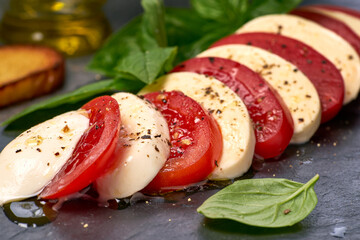 Mozzarella and tomato slices on black slate with basil and spices