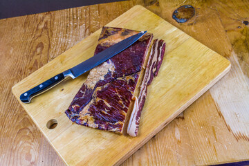 Home dry cured and smoked streaky bacon joint with knife with copyspace.