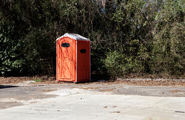 A orange portable restroom Porta potty on a vacant lot