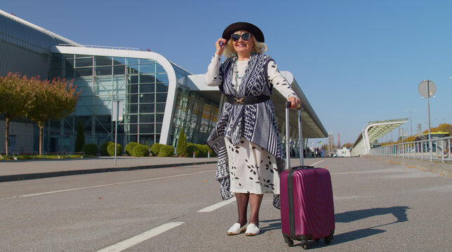 Lovely one stylish mature retired grandmother businesswoman walking with luggage suitcase bag to airport hall or railway station for boarding. Travel, vacation, journey, trip. Senior pensioner woman