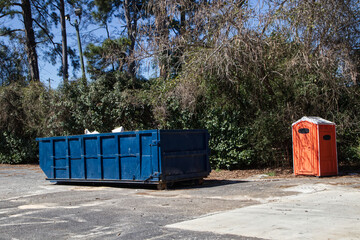 Orange porta potty and blue open top dumpster