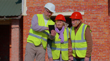 Real-estate agent selling new house to senior old couple grandmother grandfather. Male realtor showing building blueprints on digital tablet to elderly family. Aged husband and wife buying new home